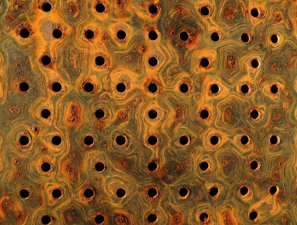 Rust corroded through metal into black voids